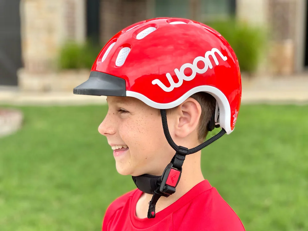 a small boy smiling while wearing the woom kids helmet